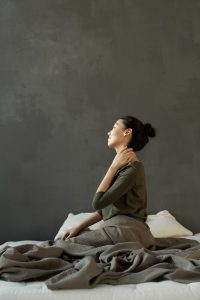 A woman sitting on top of her bed with her hands behind her neck.