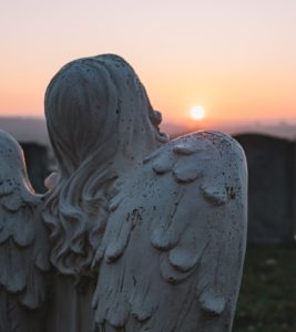A statue of an angel with wings and a sunset in the background.
