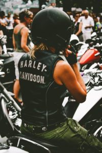 A woman in black leather jacket standing next to motorcycles.