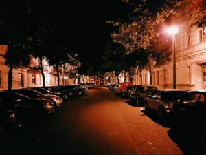 A street with parked cars and lights on the side.